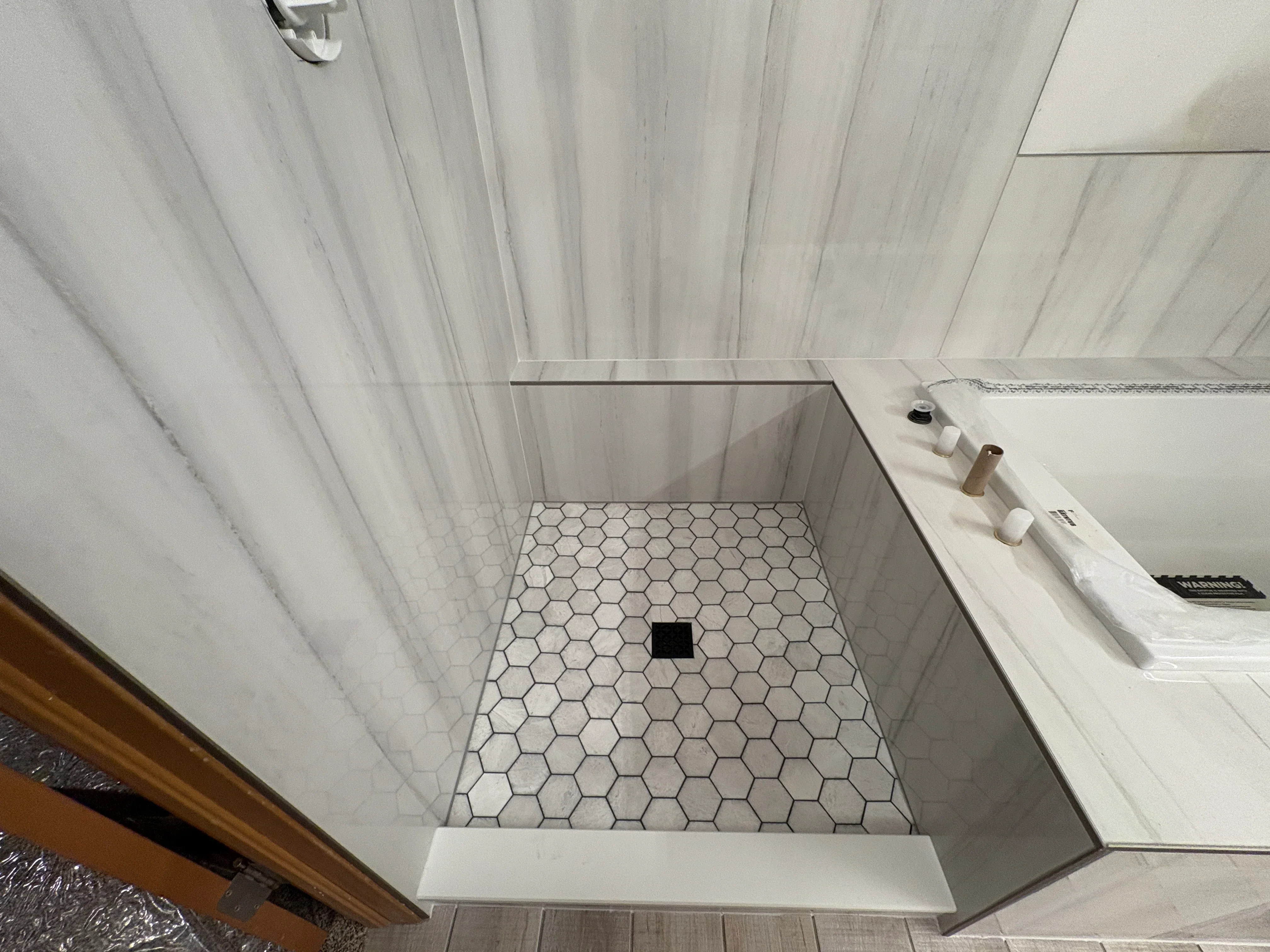 Marble hexagon tile shower floor with black drain, glass enclosure, and coordinating plank tile bathroom flooring