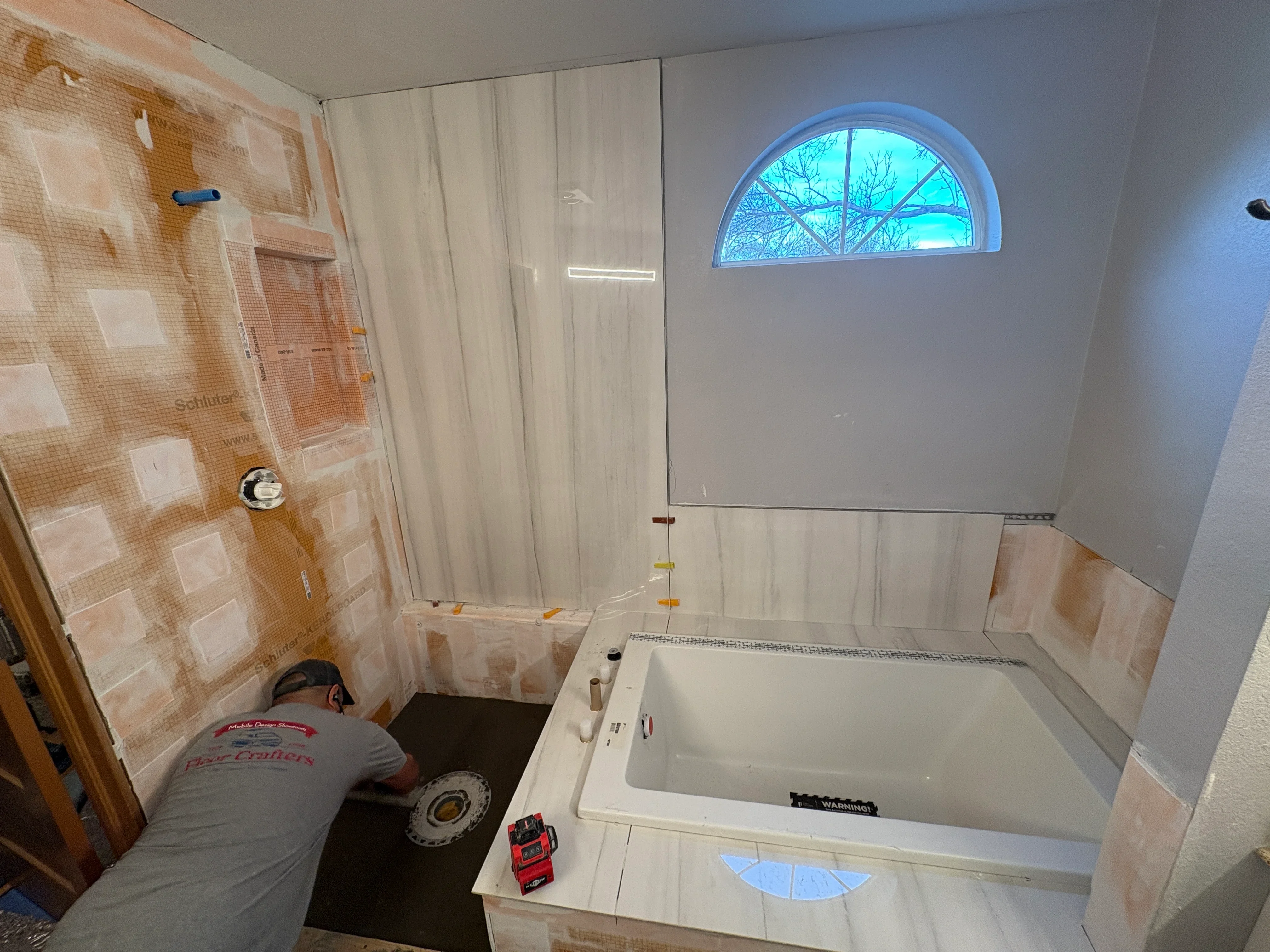 Bathroom renovation with peach ceramic tile, white soaking tub, and glass shower enclosure installation