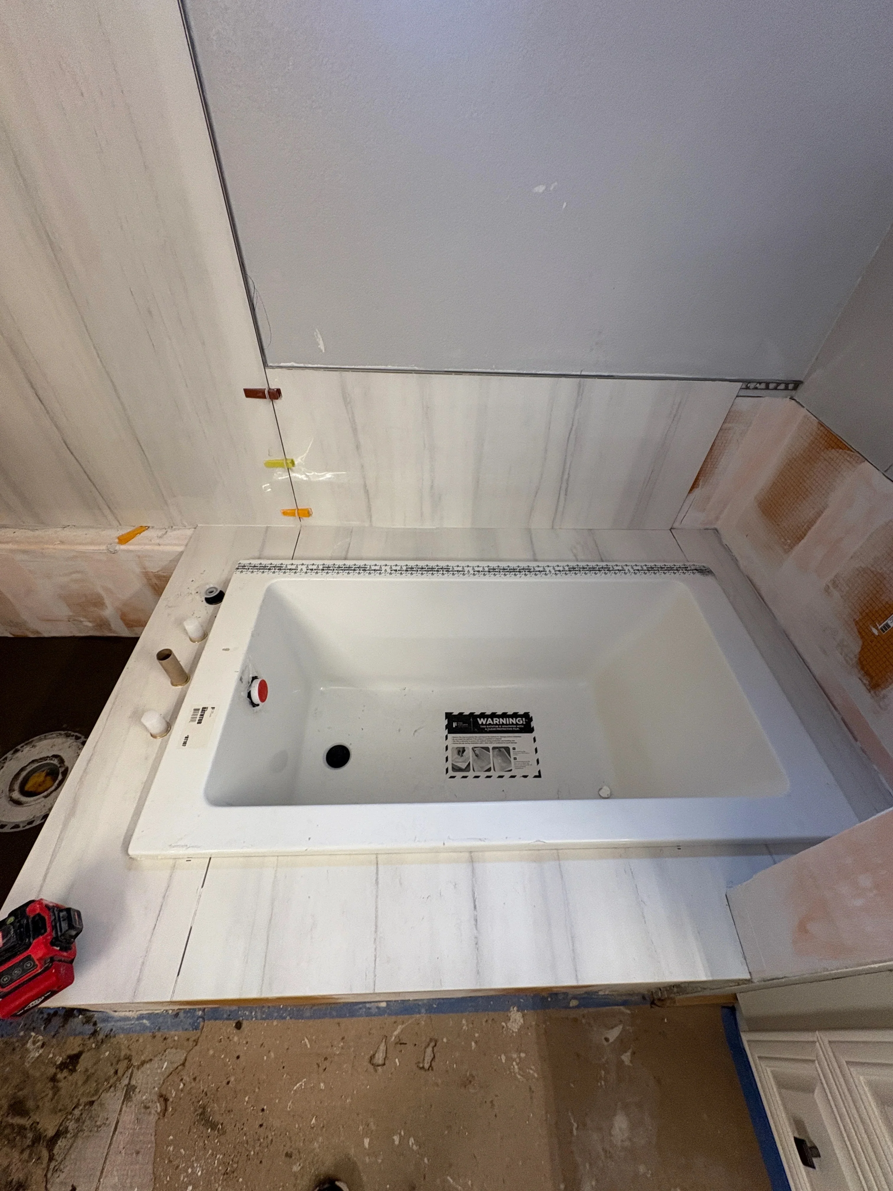 Newly installed drywall ceiling and walls with white ceramic tub and mosaic tile trim in bathroom renovation