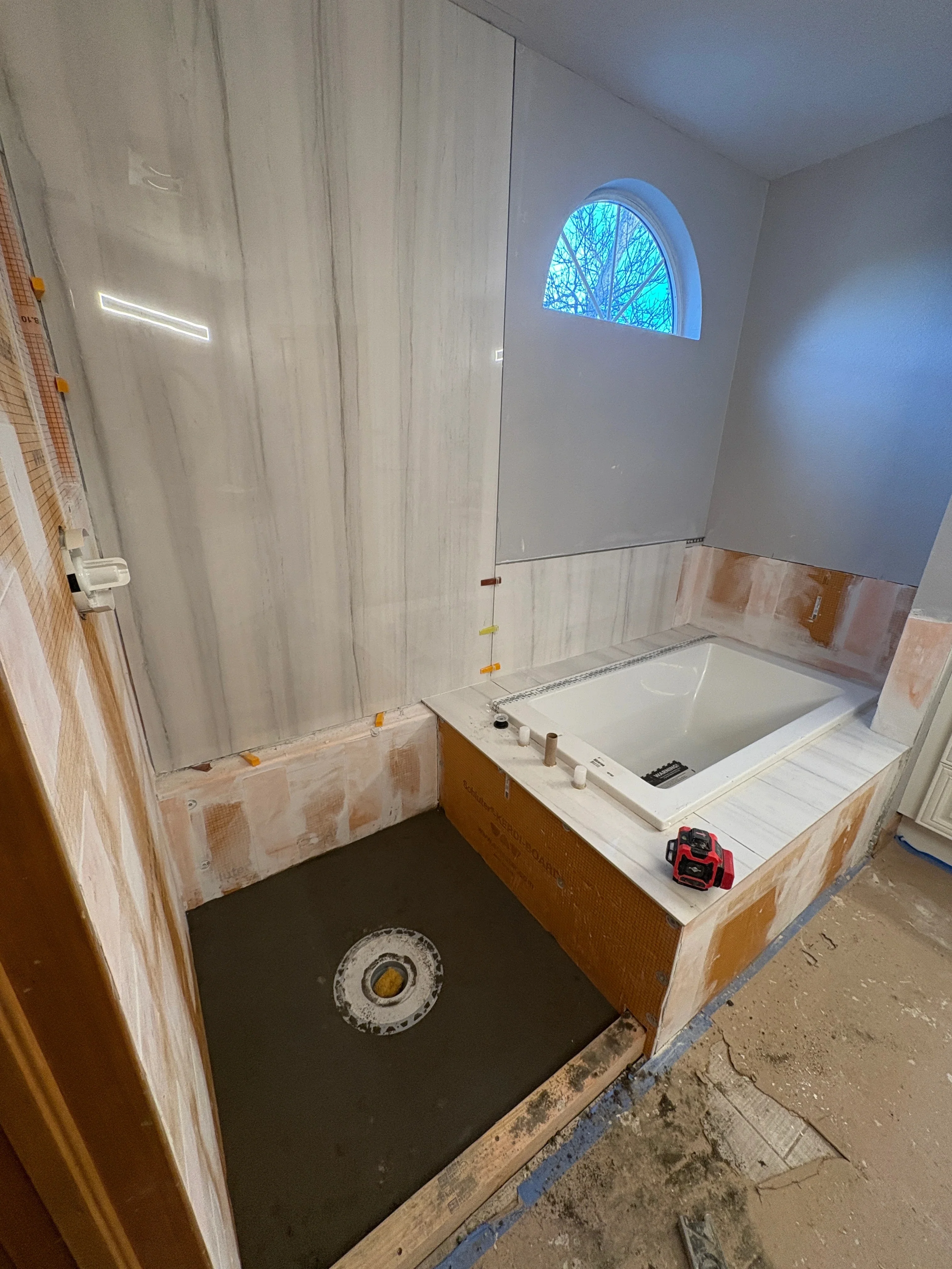 Bathroom renovation with soaking tub, waterproofing membrane, and glass shower enclosure under construction