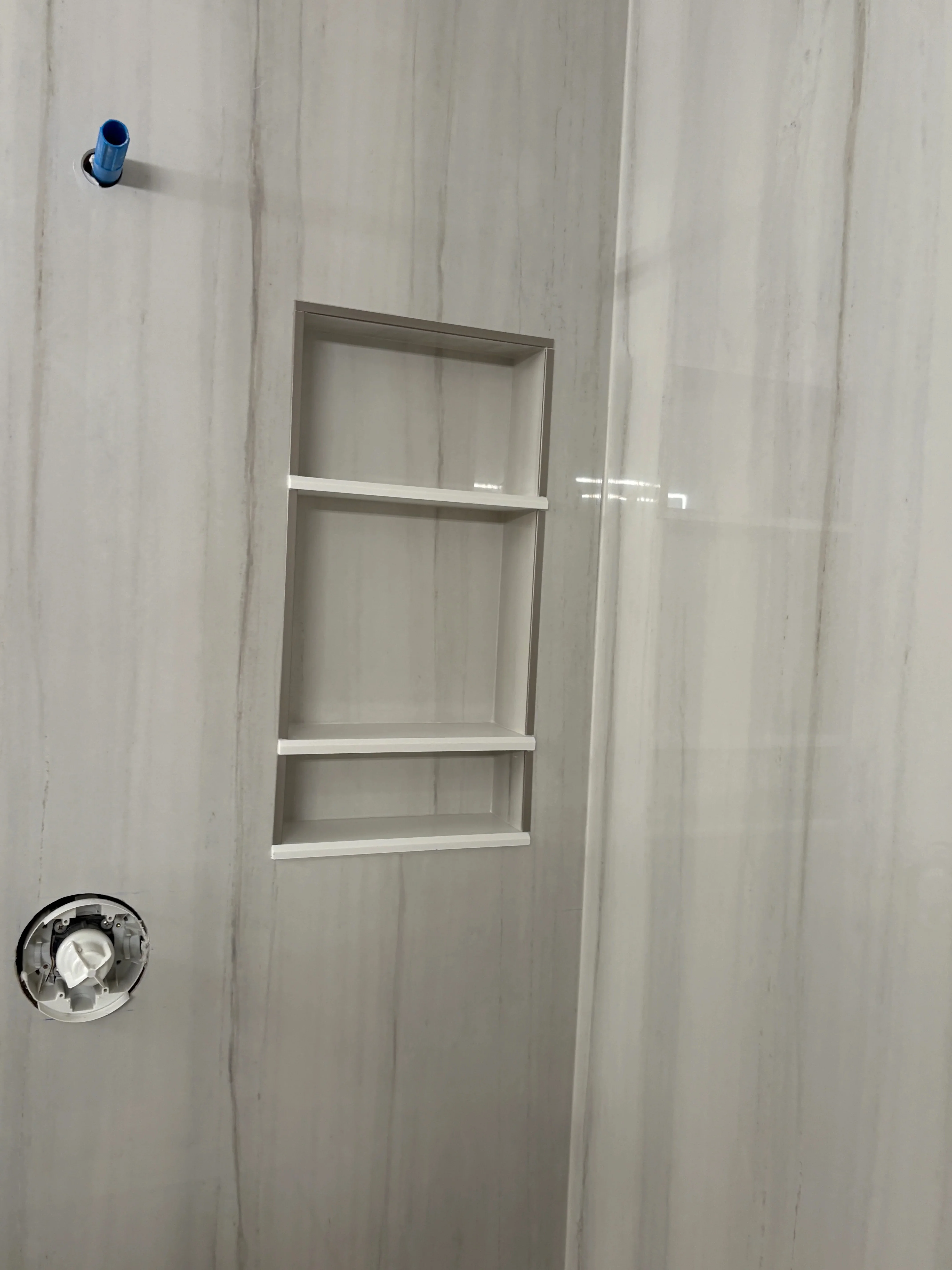 Recessed bathroom niche with three shelves and aluminum trim in finished drywall