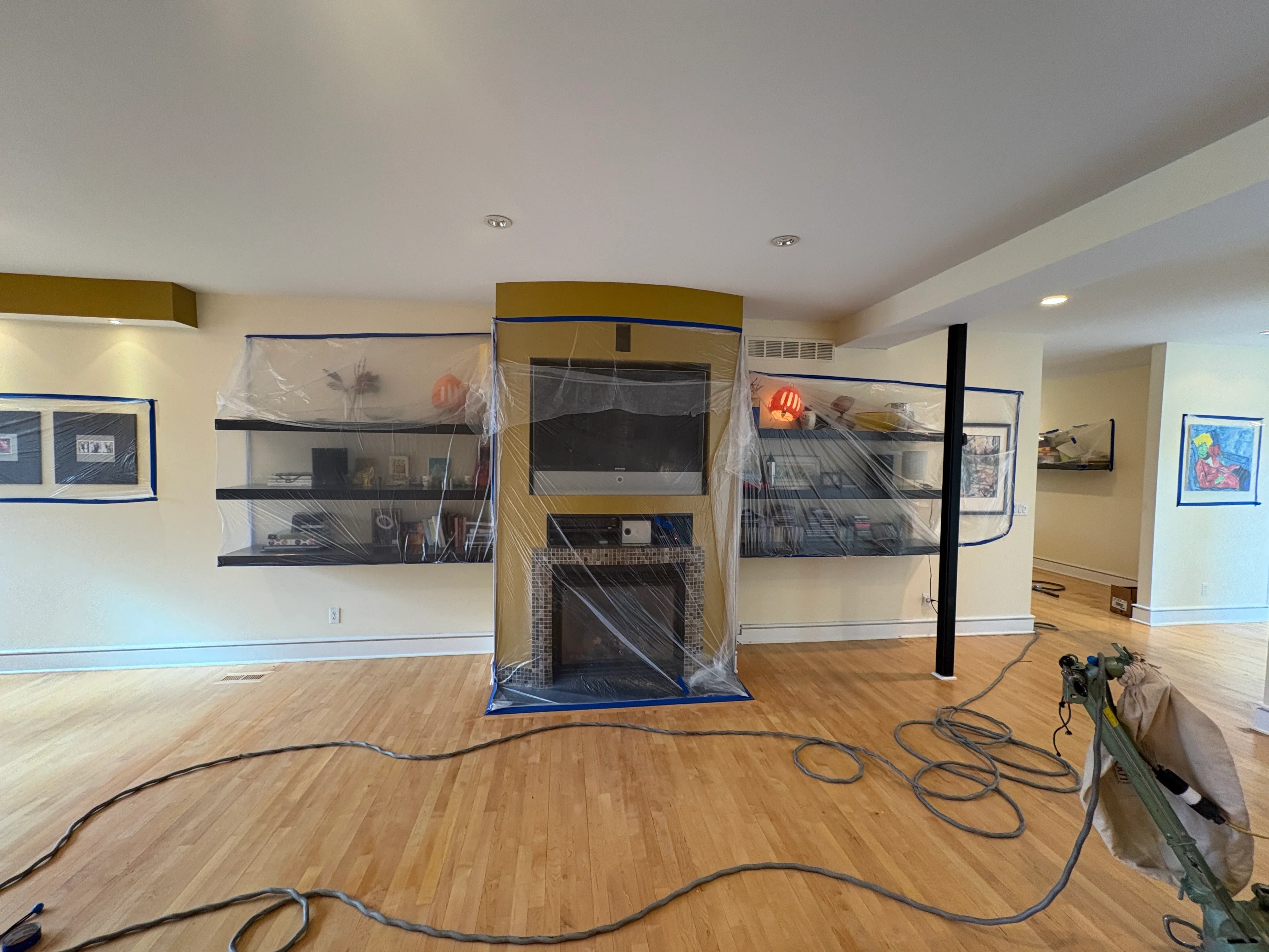 Hardwood wood plank flooring installation in progress with protective plastic covering shelving and fireplace