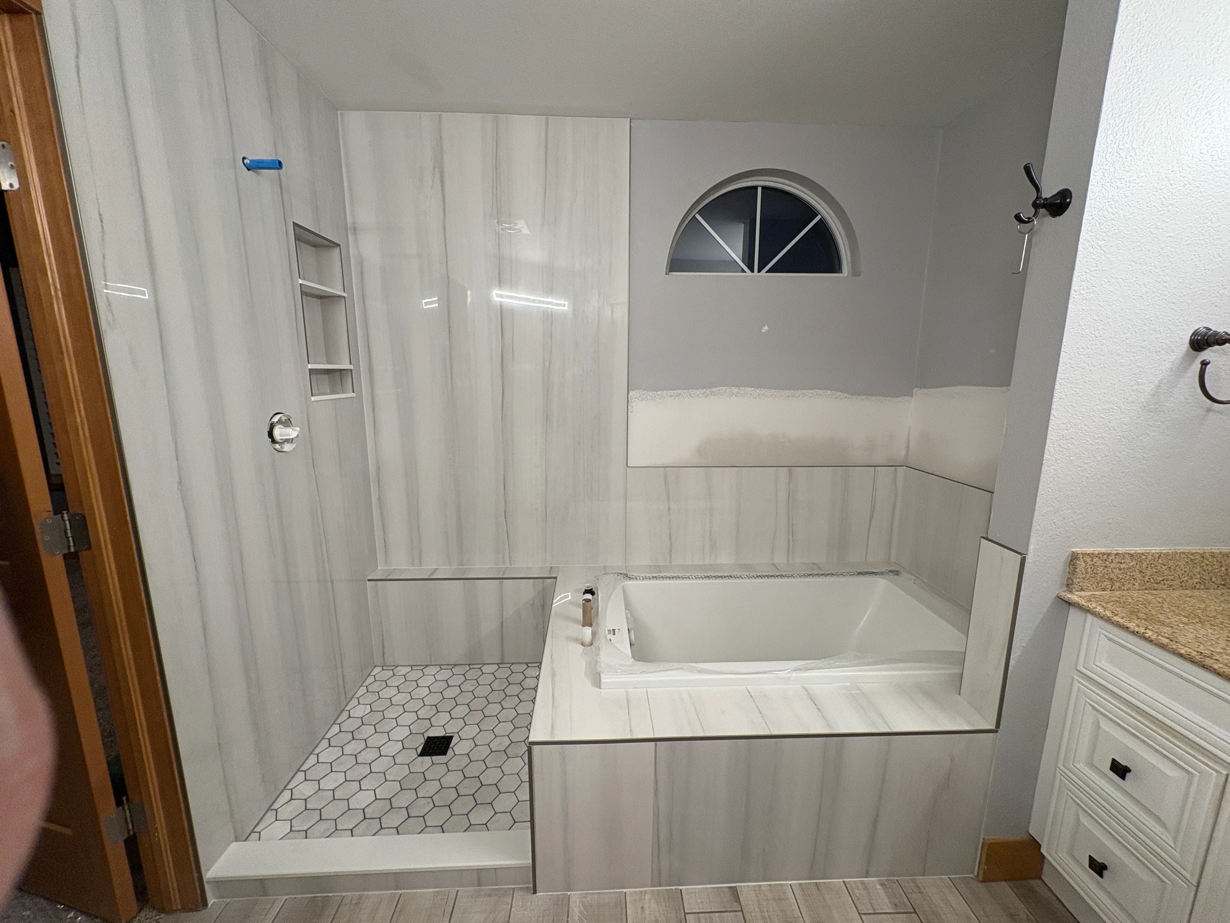 Bathroom with hexagonal tile shower floor, wood-look plank flooring, and glass shower enclosure