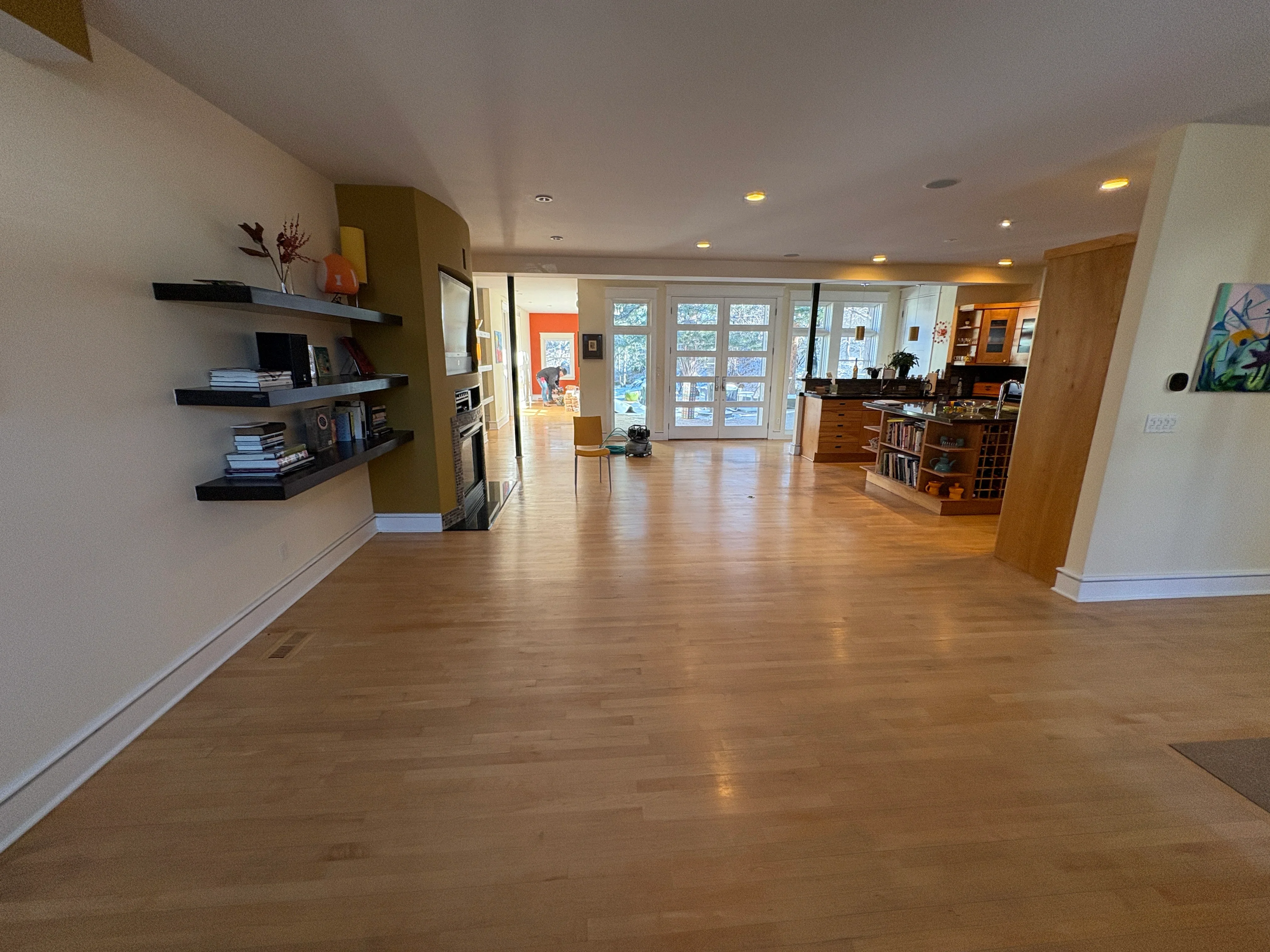 Medium-tone hardwood flooring in open concept room with white baseboards and recessed lighting