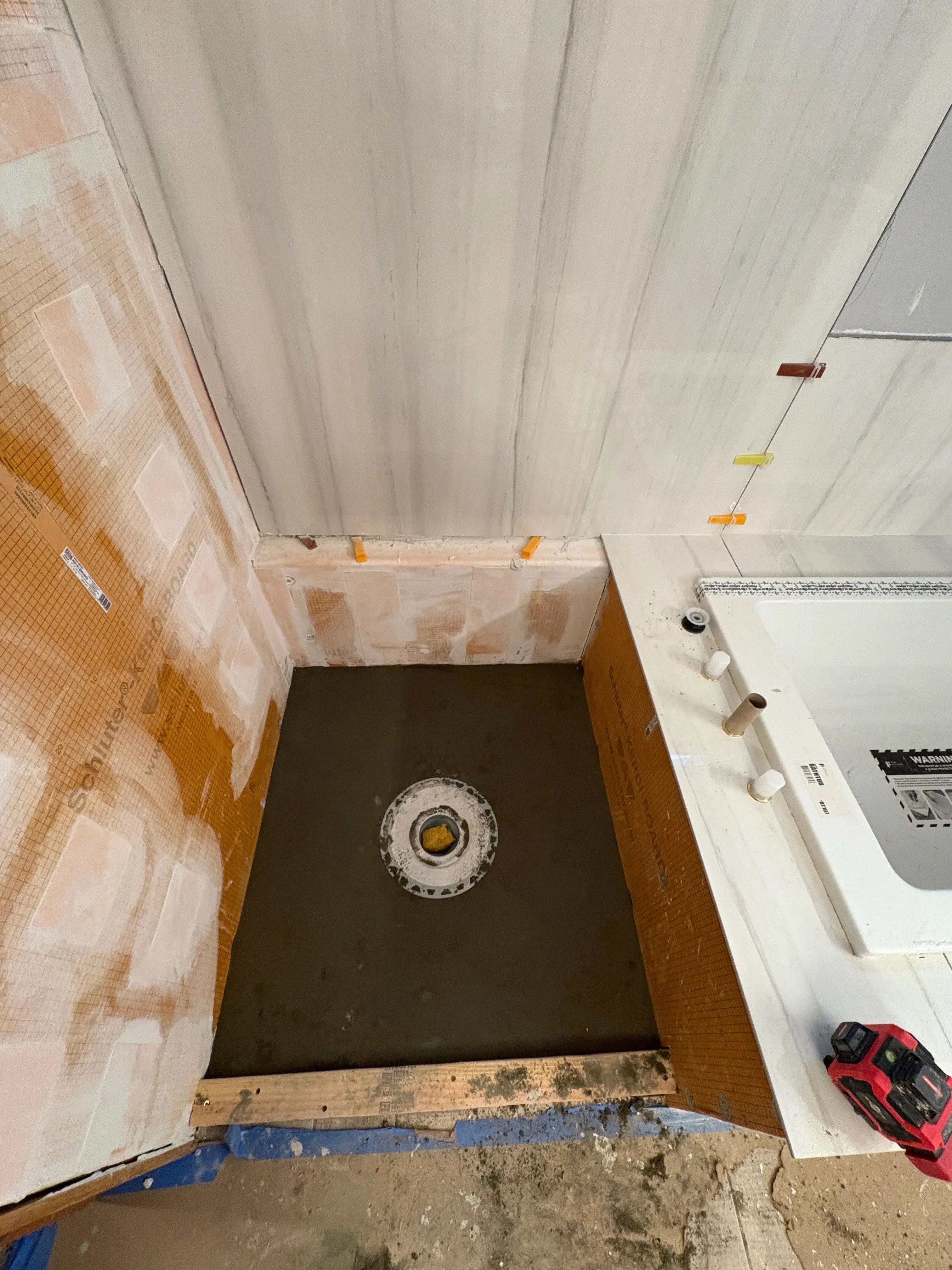 Bathroom subfloor with dark waterproof membrane, drain opening, and protective plastic sheeting during installation