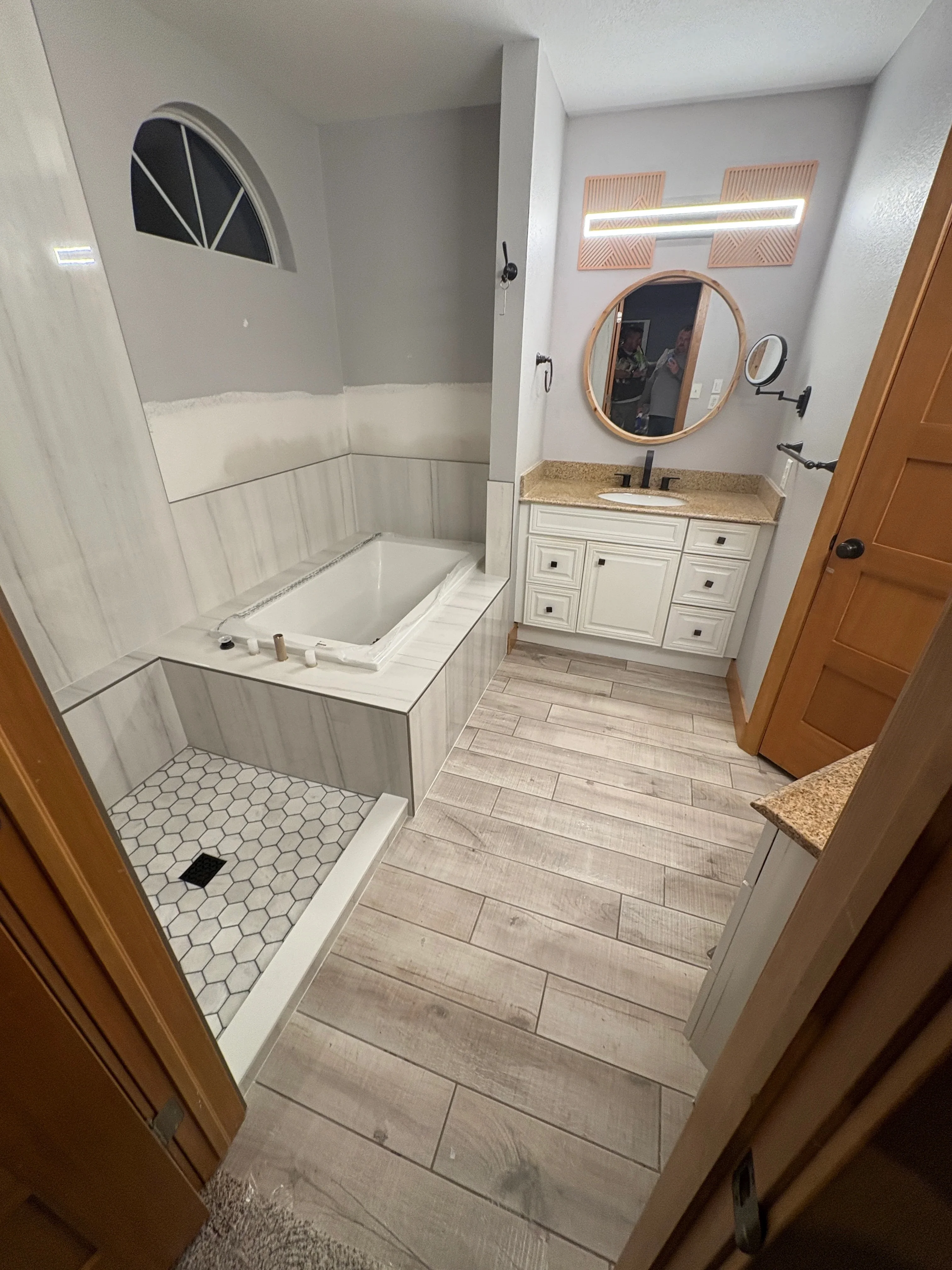 Wood plank flooring and hexagonal tile shower installation in master bathroom