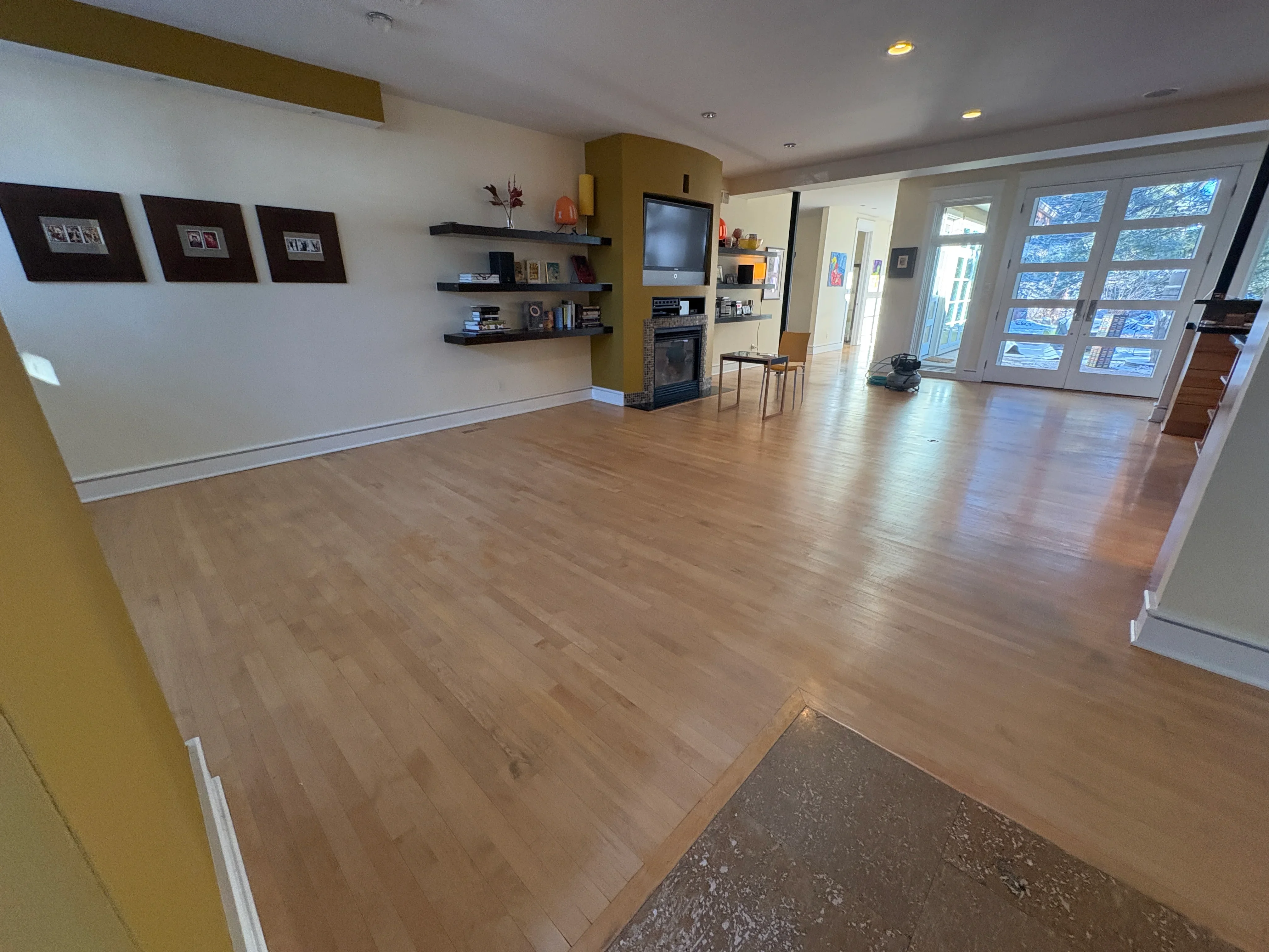 Wide-plank hardwood flooring in open living room with white baseboards and fireplace